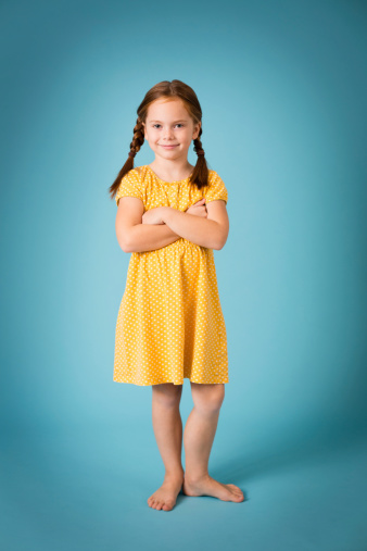 Color image of a smiling, red-haired, seven year old girl, with blue background.