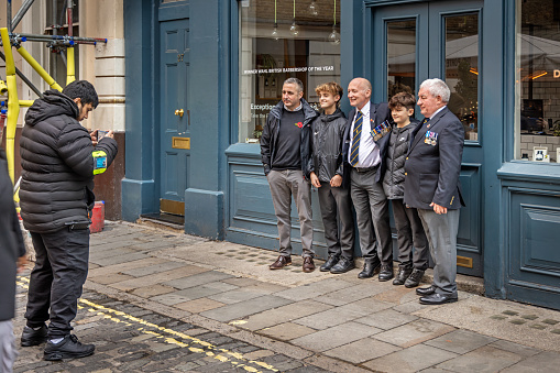 Maiden Lane, London, England - November 12th 2023:  Family group of men from different generations posing for a photo taken by a stranger outside a pub on Remembrance Day