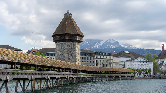 Old wooden bridge in Lucerne, with snow-capped mountains in the background, on a grey day.