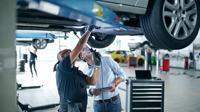 Mechanic and manager talking under car in auto repair shop