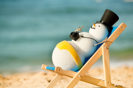 Subject: A happy snowman sunning himself on a beach chair, enjoying the sun and sand of a winter seaside tropical vacation.