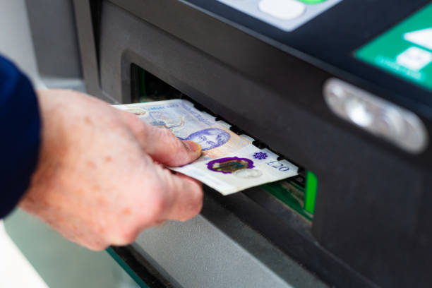 Close up of a senior man's hand using an ATM machine to withdraw cash on a city street.