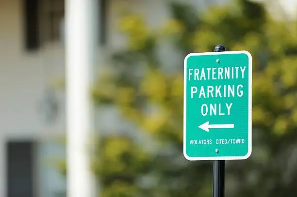 Fraternity parking only sign in front of fraternity house on university campus.