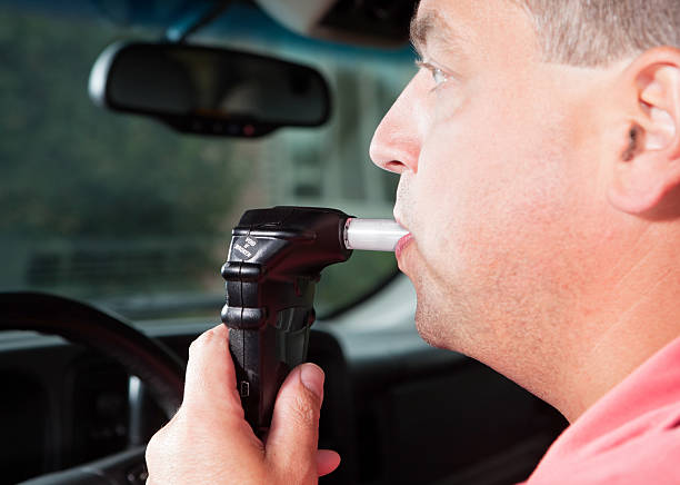 Driver Blowing into Vehicle Alcohol Ignition Interlock System A male driver is blowing into an ignition interlock system which checks his alcohol concentration before allowing the vehicle to be started. Ignition interlock devices may be an alternative sentence for drunk driving or a probation requirement for those who have received a DUI. ignition photos stock pictures, royalty-free photos & images