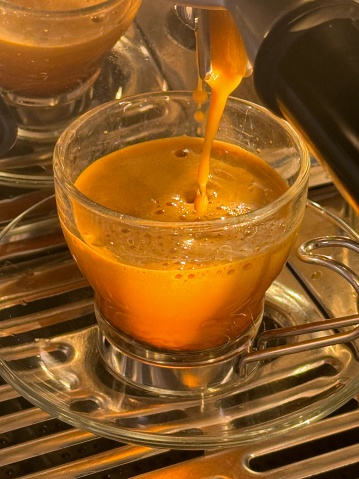 Pulling espresso shot into a glass cup in evening winter sun light