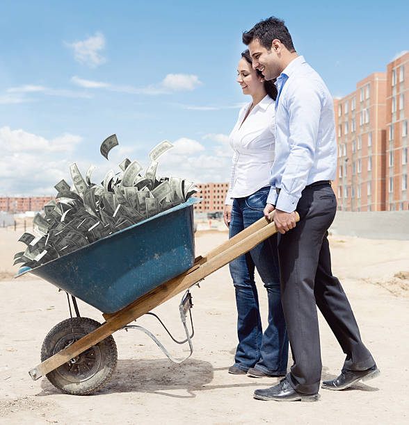 Rich couple carrying money in a wheelbarrow - savings for a house