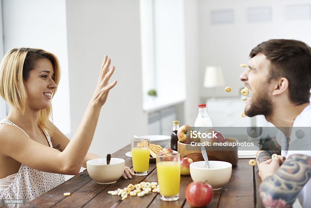 Breakfast fun Cool girl throwing some crop cereal circles and her groovy boyfriend trying to catch them with his mouth Catching Stock Photo