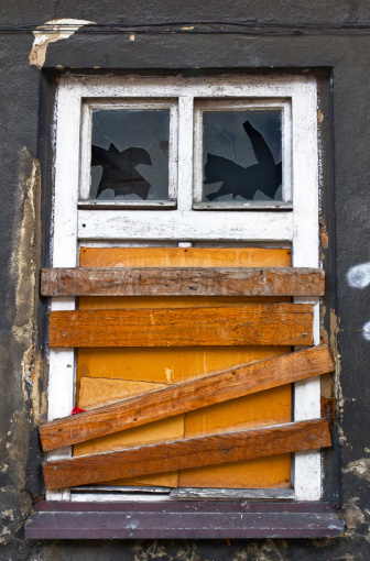 Old window with knocked out glass and boarded up.