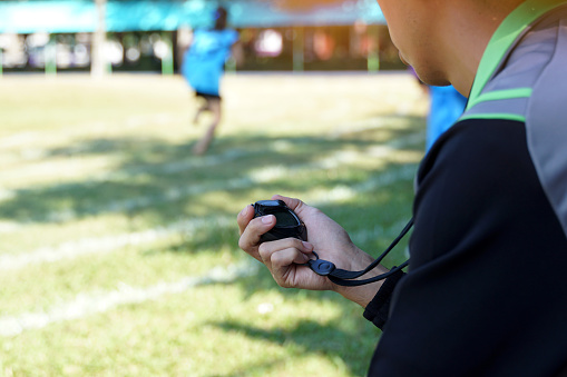 coach timed the finish line with a stopwatch to determine the winner of the school sports day running event. soft and selective focus.