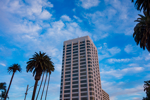 Tall white and glass building standing alone among the partly cloudy blue sky in Santa Monica California
