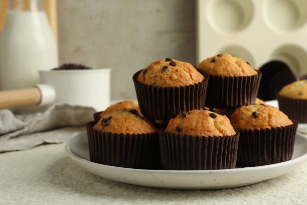 istock Delicious sweet muffins with chocolate chips on light textured table, closeup 1867627357