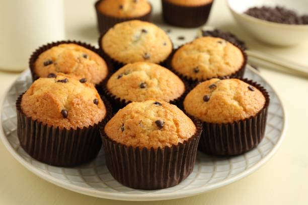 istock Delicious sweet muffins with chocolate chips on beige table, closeup 1867627360