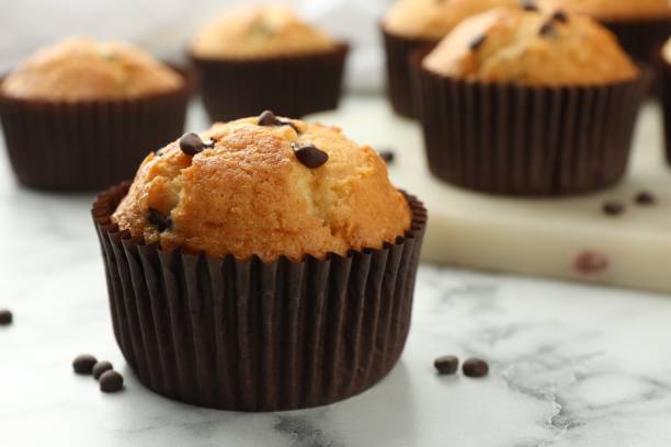istock Delicious sweet muffin with chocolate chips on white marble table, closeup. Space for text 1867628391