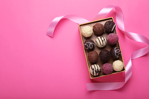 Open box with delicious chocolate candies and ribbon on pink background, top view. Space for text