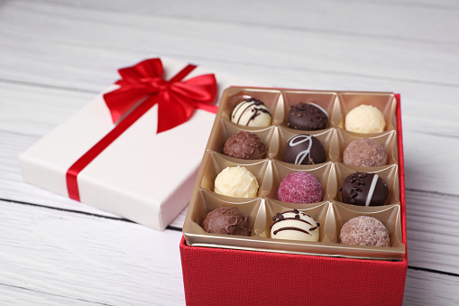 Red box with tasty chocolate candies on white wooden table, closeup