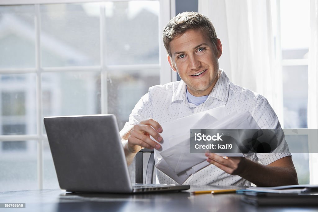 Paying bills Young man (20s) with laptop, going through mail, paying bills. Envelope Stock Photo