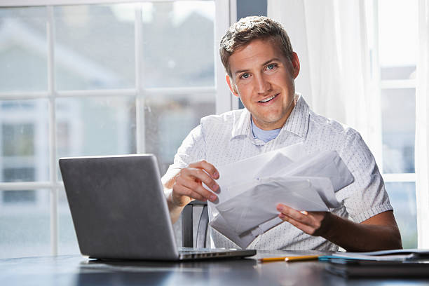 Paying bills Young man (20s) with laptop, going through mail, paying bills. Sc0601 stock pictures, royalty-free photos & images