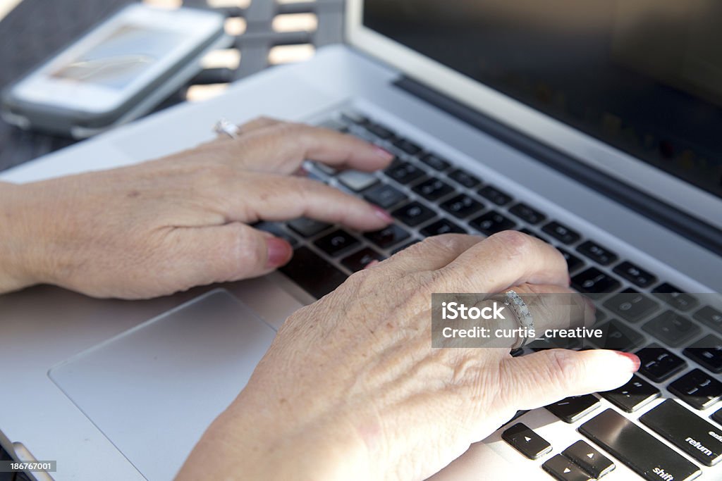 Senior donna con le mani sul portatile con cellulare - Foto stock royalty-free di 70-79 anni