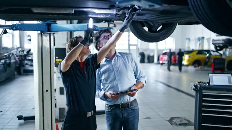 Manager approaching mechanic working under car in repair shop