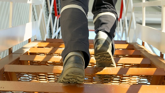 Worker uniform ascends iron ladder, industrial technology. human labor infrastructure, hands-on aspect. workers maintaining operating technological systems, modern industrial technology. Vertical