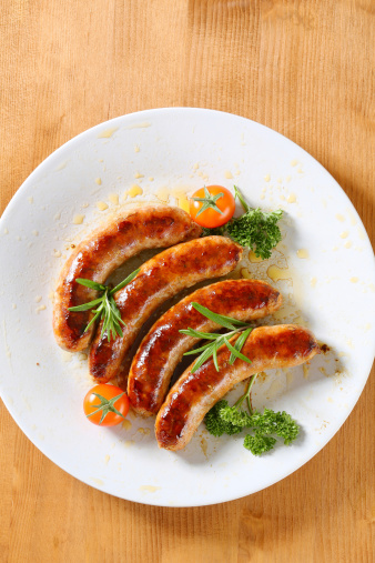 roasted white sausages garnished with cherry tomatos, parsley and rosemary on white plate