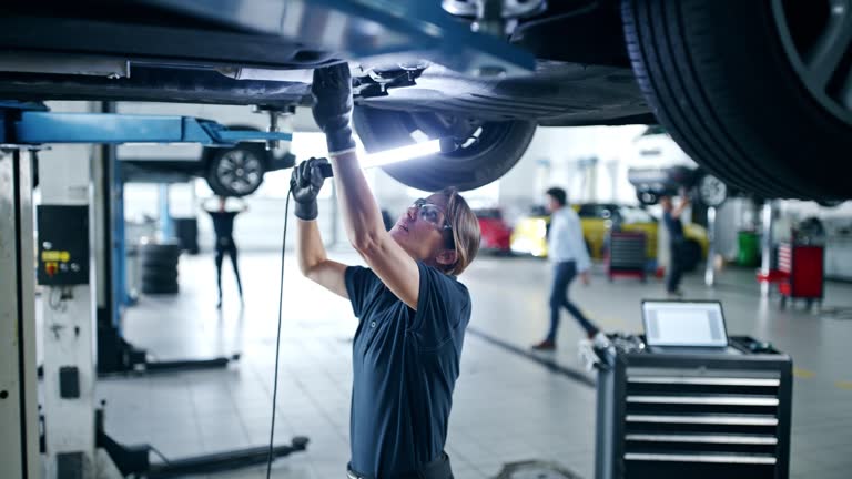 Female mechanic with light examining car chassis in auto repair shop