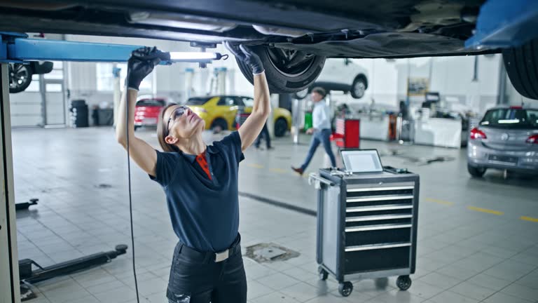 Female mechanic with light examining chassis of car in repair shop