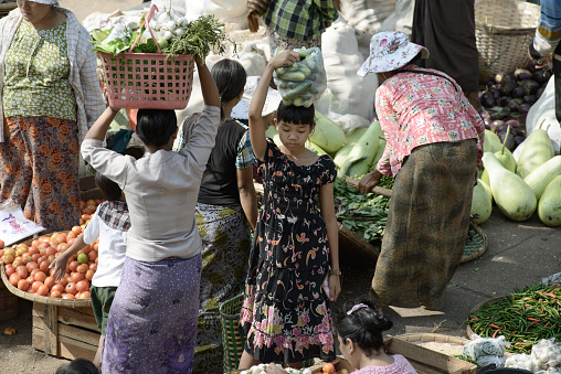 02/22/2014 - Yangon, Myanmar: People buying and selling fresh vegetables at a bustling outdoor market in Yangon, Myanmar, with a focus on traditional methods of carrying goods
