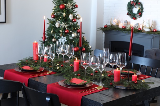 Elegant Christmas table setting with dishware and burning candles in festively decorated room