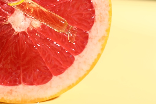 Dripping cosmetic serum from pipette onto grapefruit slice against yellow background, top view. Space for text