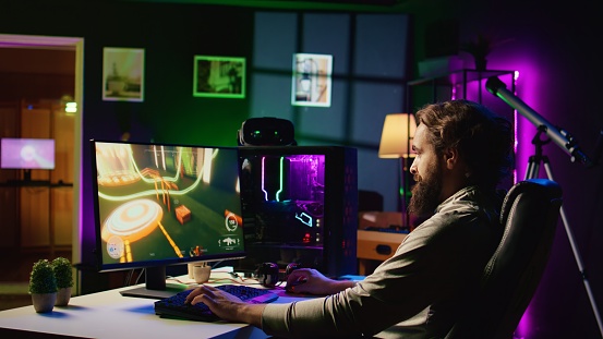 Man in dark living room playing science fiction videogame on gaming PC, relaxing by shooting enemies. Gamer battling flying robots in online singleplayer shooter from rgb lights ornate house