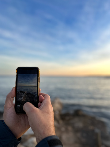 Man’s hands holding a mobile phone photographing the sunset