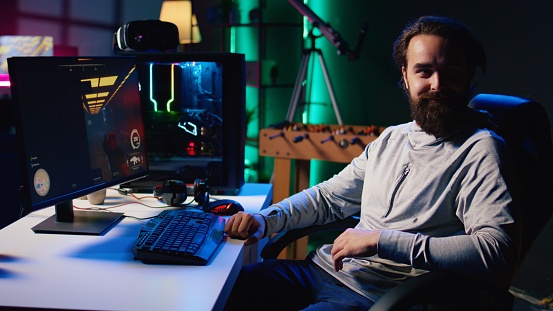 Portrait of cheerful man playing first person shooter videogame with automatic gun shooting laser bullets at flying robotic foes. Smiling gamer competing in PvP online multiplayer game