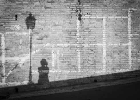 Shadow of lamp and photographer on ancient brick wall. Black and white.