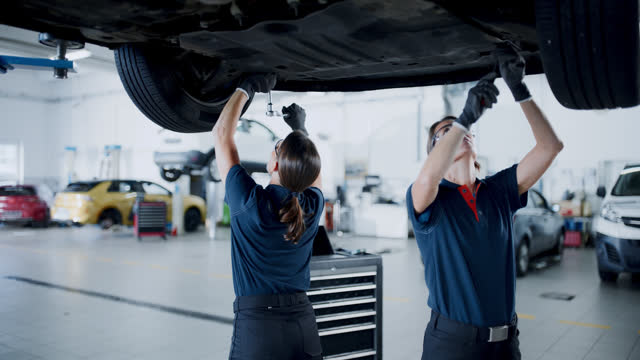 Female maintenance engineers working under car in repair shop