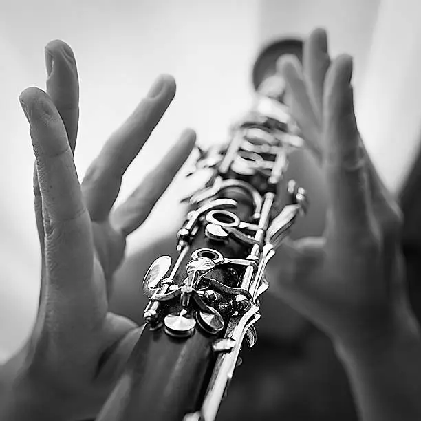 Clarinet in hands of woman musician. Black and white images with increase of contrast and some texture. Square image.