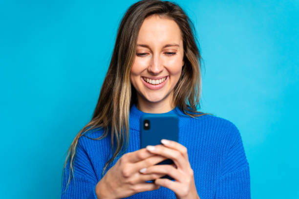 istock Happy young woman using mobile phone on a blue background with copy space 1867789711