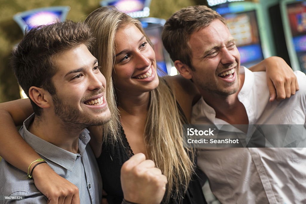 Sorrindo amigos no cassino ganhar nos caça-níqueis. - Foto de stock de Abraçar royalty-free