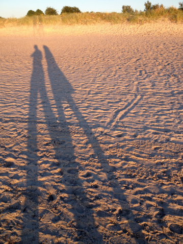 Long shadows of two people on a sand beach in Malmo, Sweden at sunset.  Captured with iPhone4S.
