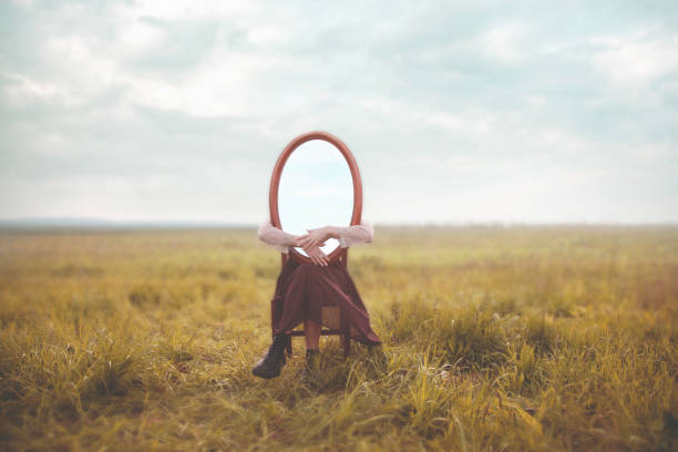 woman hides holding a mirror in front of her face; introspection path concept