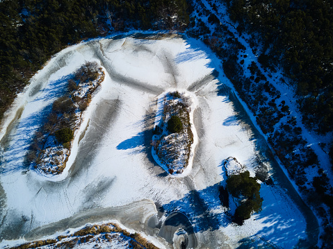 Aerial view of idyllic frozen lake surrounded with trees in forest and landscape on sunny day