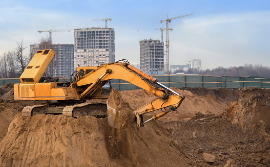 Excavator on groundwork on construction site. Backhoe dig foundation for house construction. Excavation works on building    construction. Excavator Machinery on earthworks. Tower crane in build.