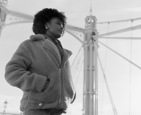 Nostalgic black and white portrait of young black woman standing under bridge structure. It is cold morning day. Image made with analog medium format camera.