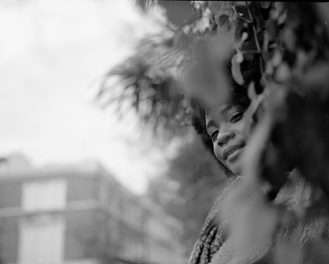 Black and white portrait of young black woman hidden by brushes in the street. It is an analog image made with a medium format camera.