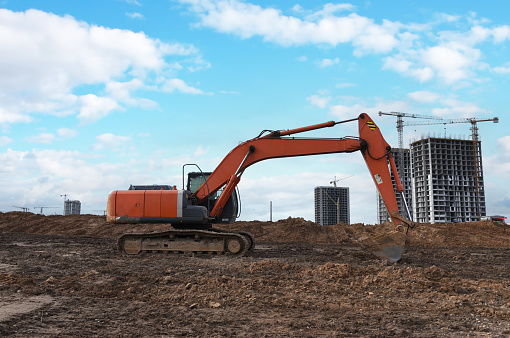 Construction site. Excavator on groundwork. Backhoe dig foundation for house construction. Excavation works on building    construction. Excavator Machinery on earthworks. Tower crane in build.