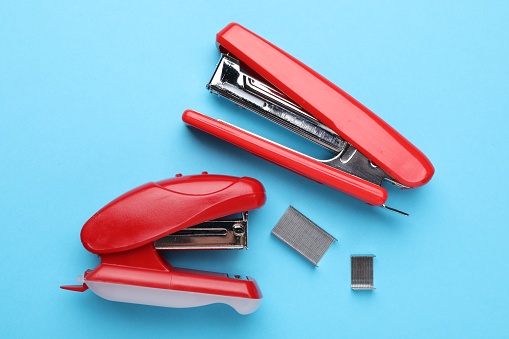 Bright staplers with staples on light blue background, flat lay