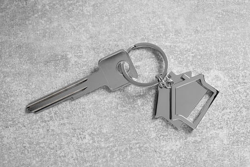 Key with keychain in shape of house on light grey table, top view