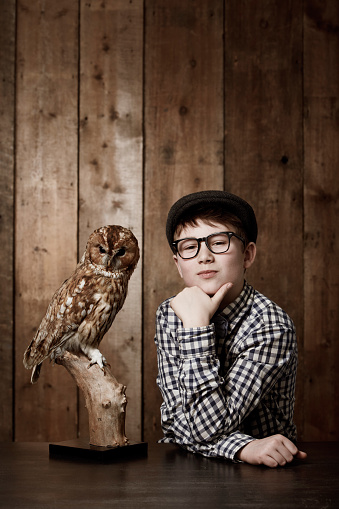 Young boy in retro clothing wearing spectacles with a thoughtful expression alongside an owl