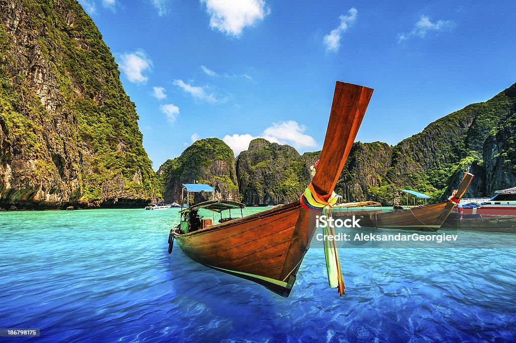 A Longtail Wooden Boat at Maya Bay, Thailand Long tail wooden boat at Maya Bay on Ko Phi Phi Le, made famous by the movie titled "The Beach". Beautiful cloudscape over the turquoise water and green rocks in Maya Bay, Phi Phi Islands, Thailand. Phuket Province Stock Photo