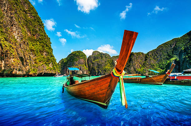 A Longtail Wooden Boat at Maya Bay, Thailand Long tail wooden boat at Maya Bay on Ko Phi Phi Le, made famous by the movie titled "The Beach". Beautiful cloudscape over the turquoise water and green rocks in Maya Bay, Phi Phi Islands, Thailand. phi phi islands stock pictures, royalty-free photos & images